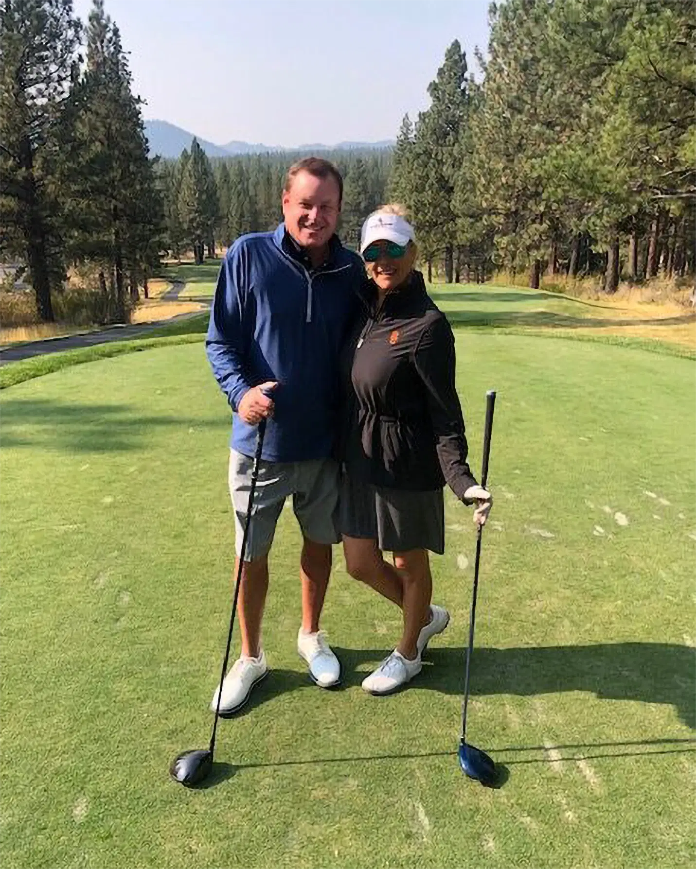 Devin Doyle and his wife posing with golf clubs on a tree-lined golf course