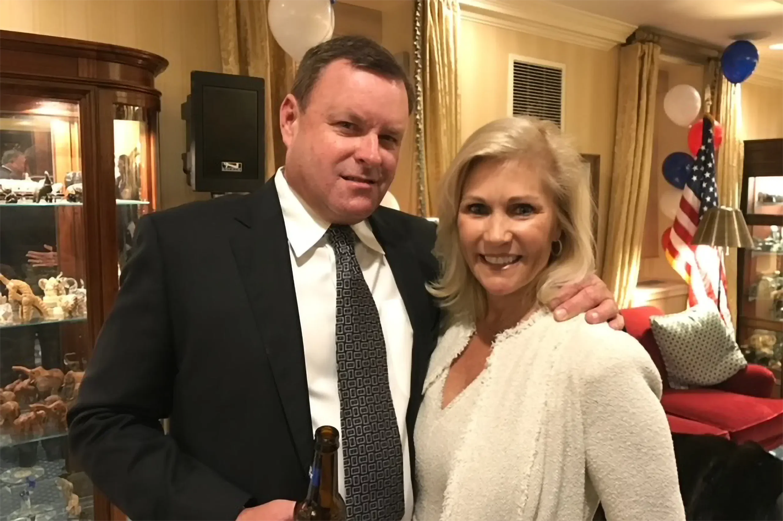 Devin Doyle and his wife posing at an indoor celebration with red, white, and blue balloons