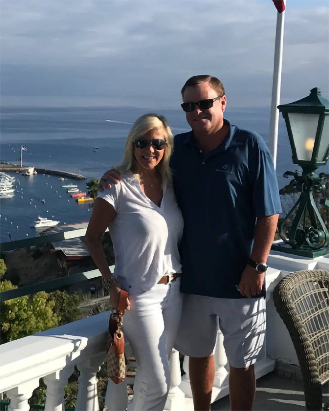 Devin Doyle and his wife posing on a terrace overlooking a marina and the ocean